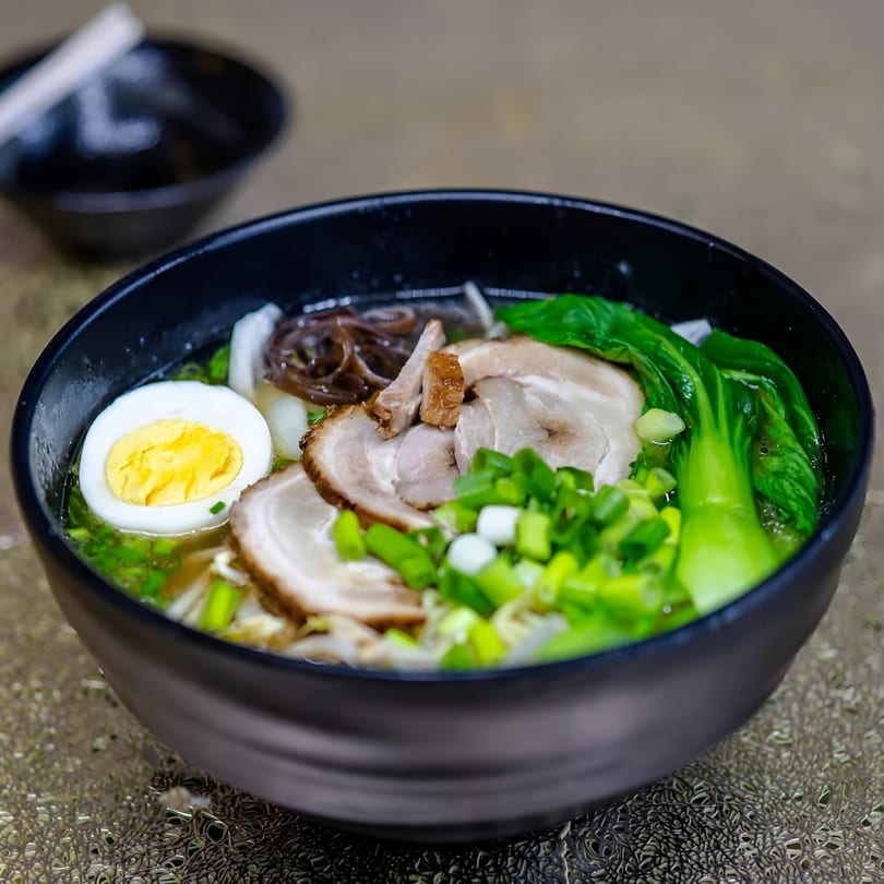 A black bowl of Jackpot Teriyaki ramen with pork, egg, bok choy, and green onions.
